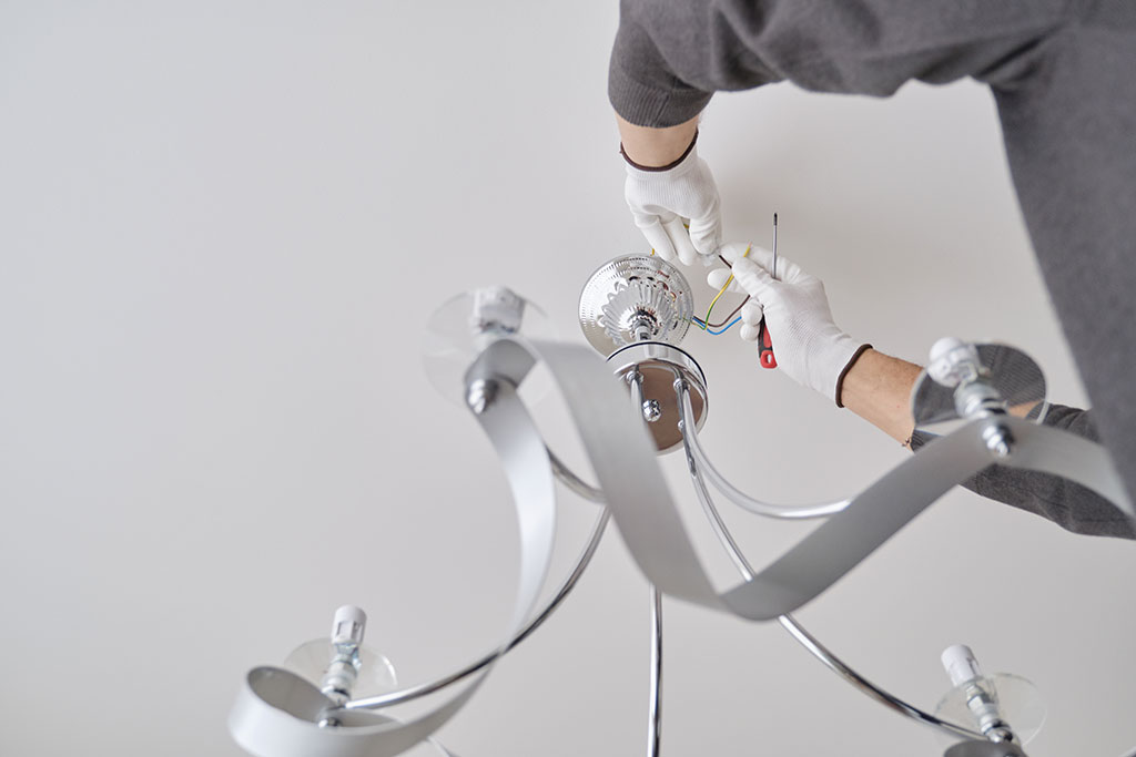 Installation ceiling lamp, hands of male electrician fixing chandelier with use of professional tools